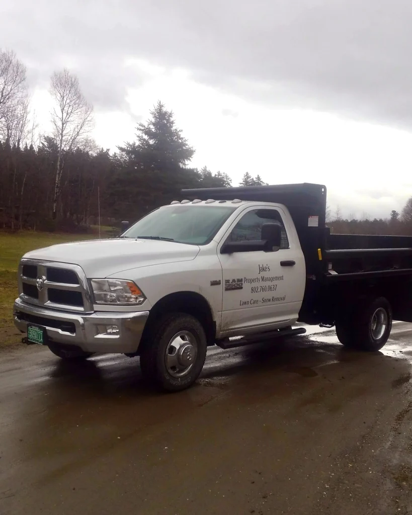 a white jake's property management ram truck with an industrial sized bed on a damp dirt road