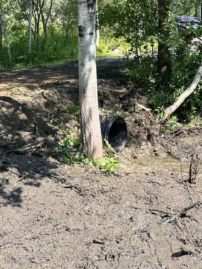 end of portfolio a new culvert pipe running under a dirt road, the ground is muddy