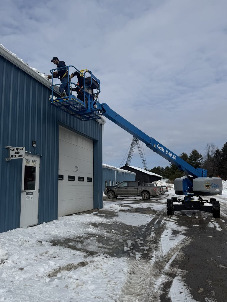 man-lifter raising workers to the gutters of a blue warehouse