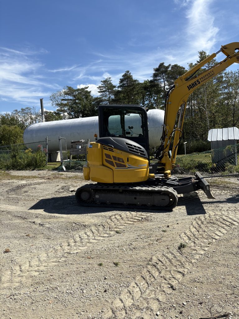 excavator in front of large gas tank