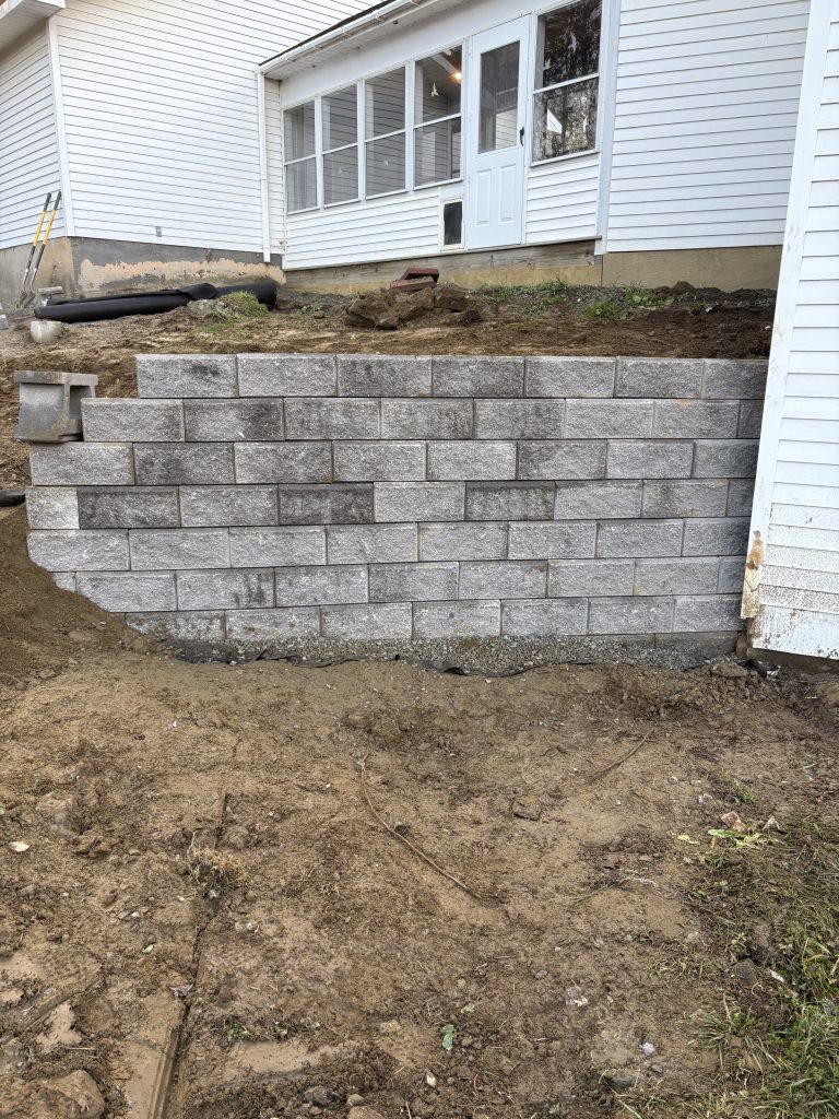 a nearly completed retaining wall in front of a white house