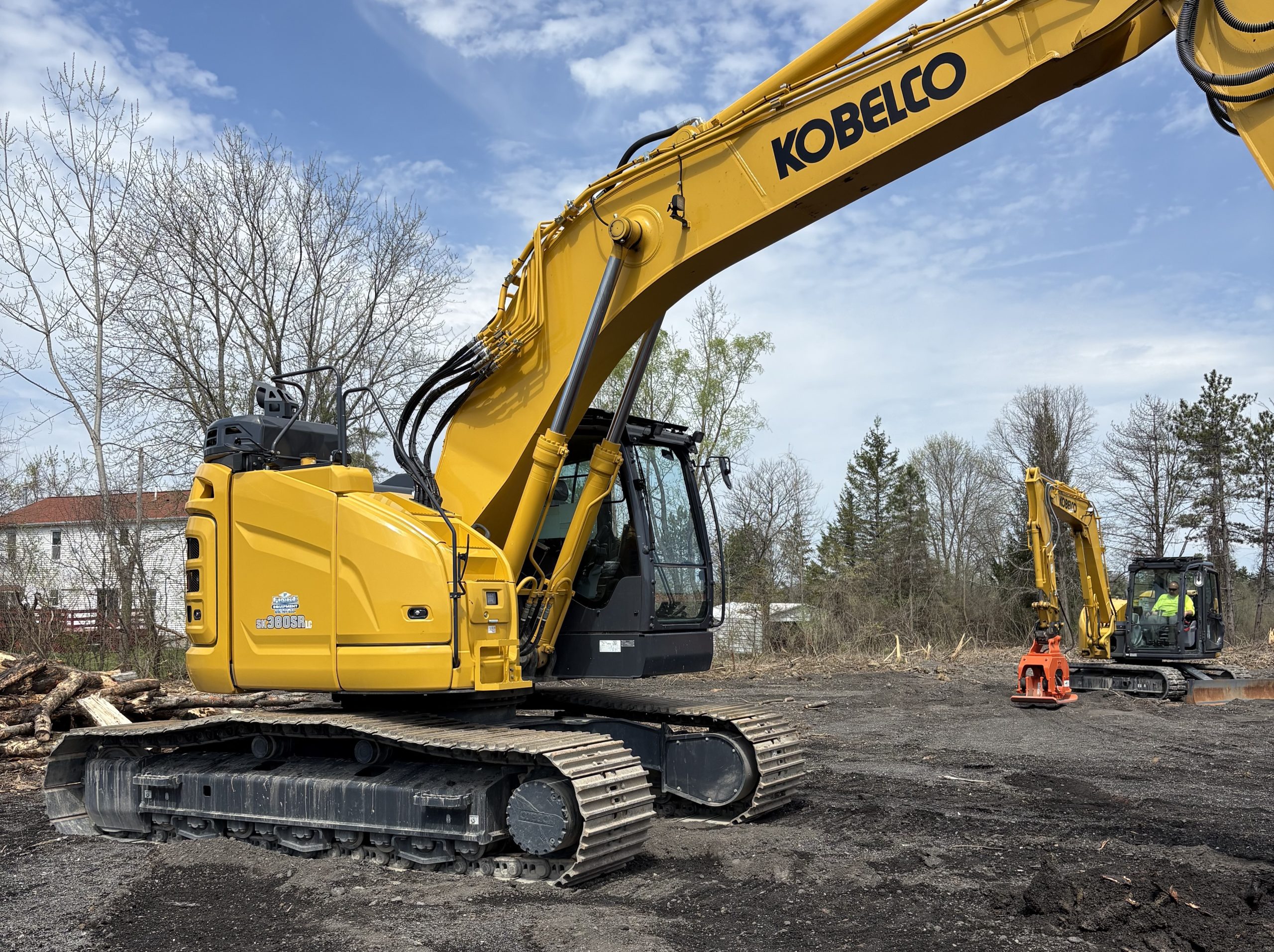 kobelco excavator with a tamping machine operated by a man in the background